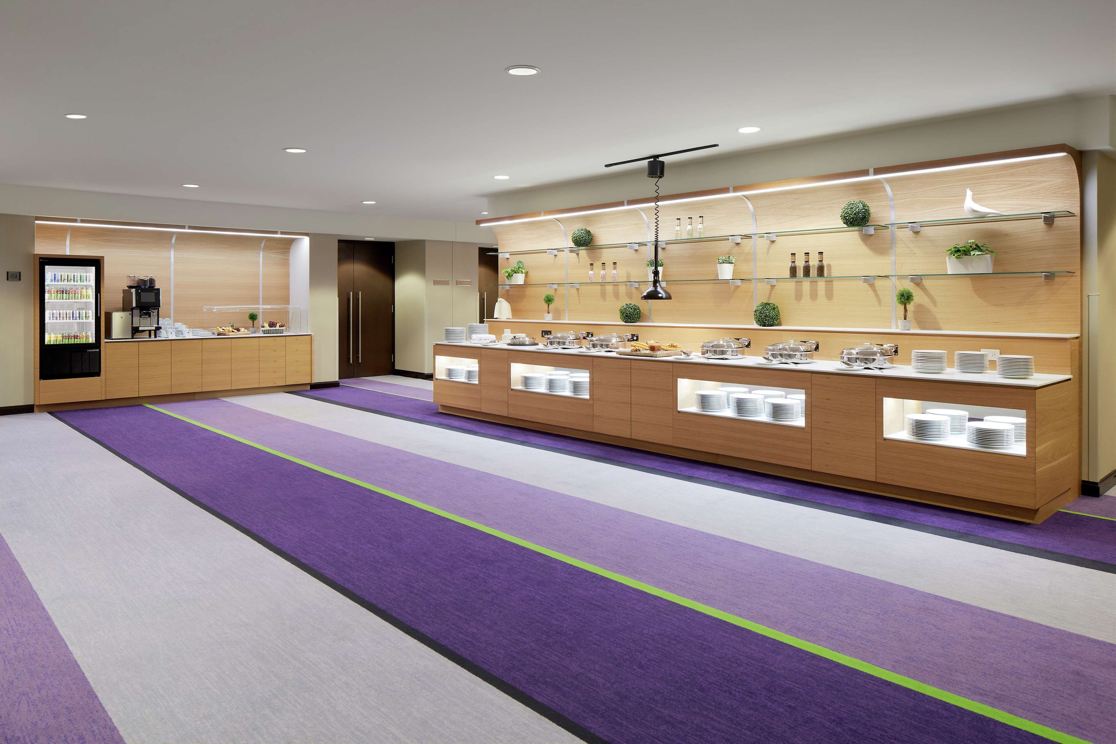 Un moderno vestíbulo de hotel con un mostrador de recepción, un refrigerador y una zona de estar con alfombra púrpura.