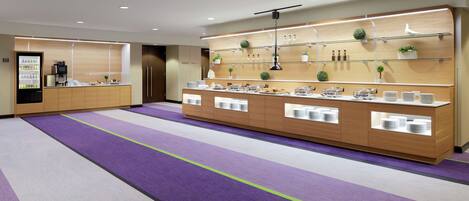 Un moderno vestíbulo de hotel con un mostrador de recepción, un refrigerador y una zona de estar con alfombra púrpura.