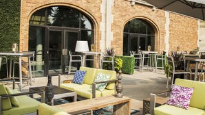An outdoor patio area with green seating, a wooden table, and a brick building in the background. - Delta Hotels by Marriott Bessborough (Saskatoon)