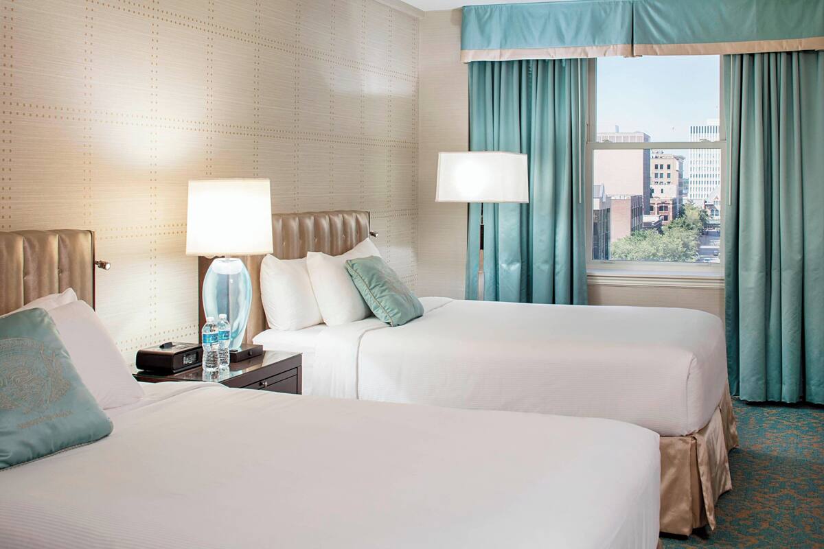 Quarto de hotel com duas camas, janela com cortinas e vista para a cidade.