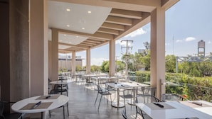Un café en plein air avec des tables et des chaises, de grandes fenêtres et une vue sur la ville.