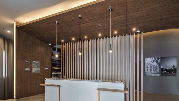 Un espace d’accueil doté d’un plafond en bois, de luminaires suspendus, d’un comptoir de réception et d’un mur à lattes verticales.