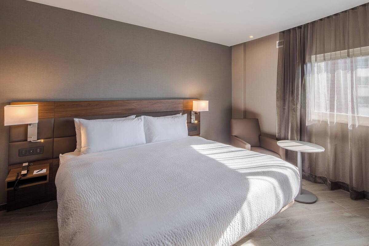 Une chambre d’hôtel moderne avec un grand lit, des lampes de chevet, une petite table ronde et un canapé.