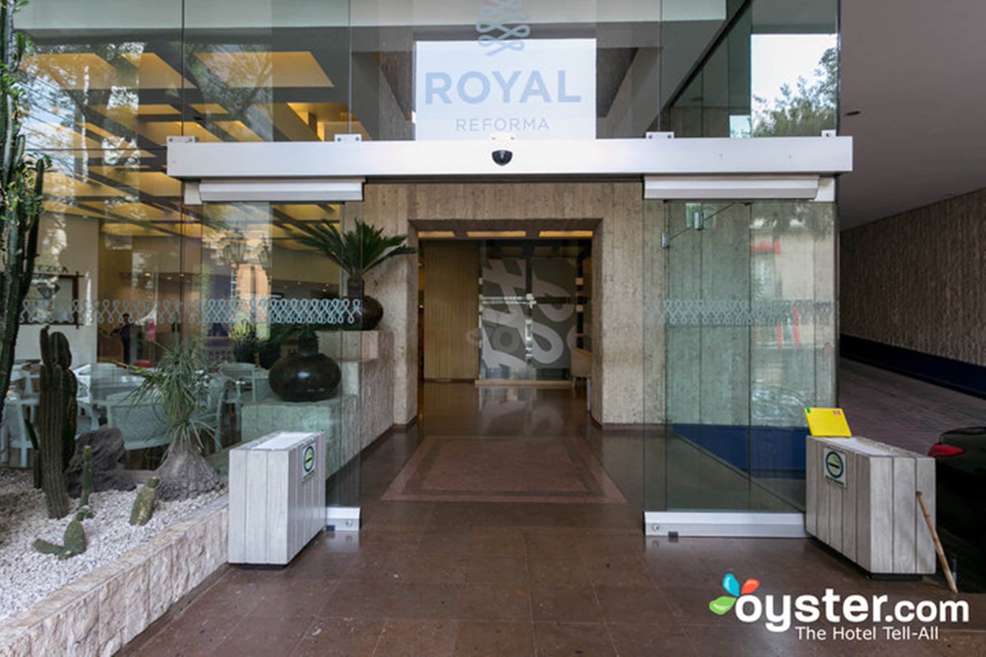 The entrance of a hotel named 'ROYAL REFORMA' with a modern design, glass doors, and a small reception desk.