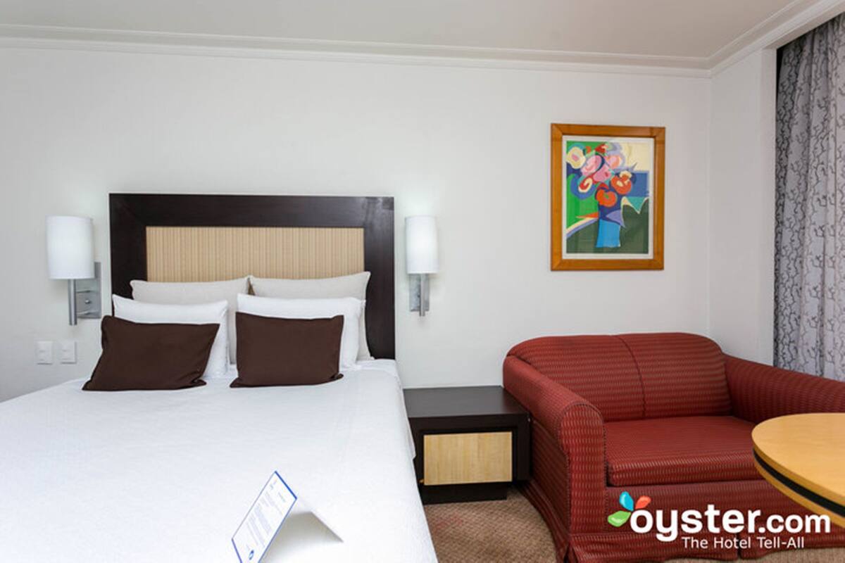 Quarto de hotel com cama, sofá vermelho, uma mesinha e um quadro na parede.