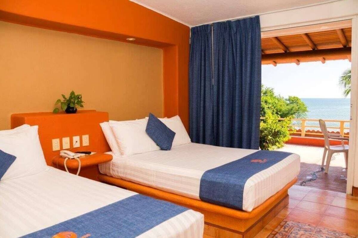 A hotel room with two beds, a view of the ocean, and a balcony with a chair.