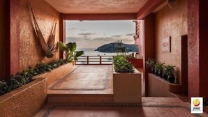 A room with a view of the sea and mountains, featuring a concrete floor, potted plants, and a wooden railing. - Hotel Irma (Zihuatanejo)