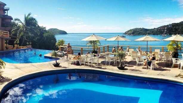 A poolside area with lounge chairs and umbrellas, overlooking a body of water and hills. - Hotel Irma (Zihuatanejo)