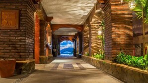 A corridor with brick walls, potted plants, and a view of the sea. - Hotel Irma (Zihuatanejo)