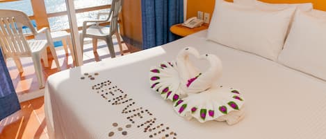 A hotel room with a bed, a balcony with chairs, and a view of boats on the water.