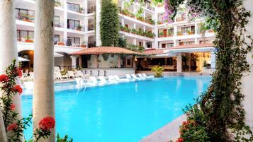 Un hotel de varios niveles con una piscina central rodeada de sillones de descanso y plantas en macetas.