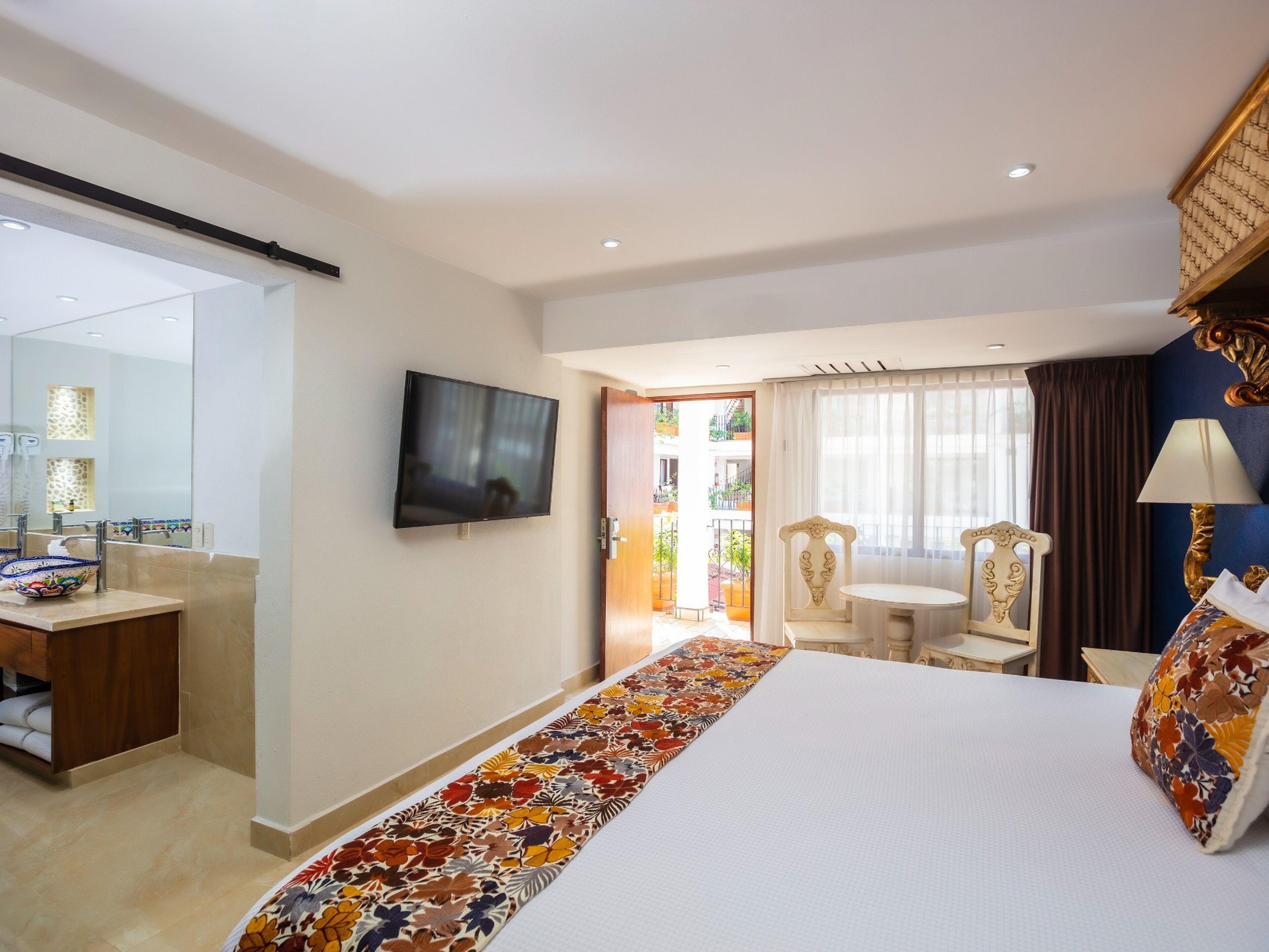 A hotel room with a bed, a TV, a desk, a chair, and a view of the outside.