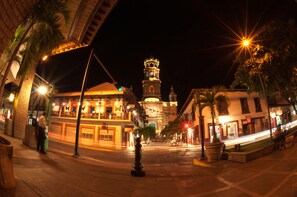 A nighttime street view with a prominent clock tower, illuminated buildings, and a pedestrian crossing.