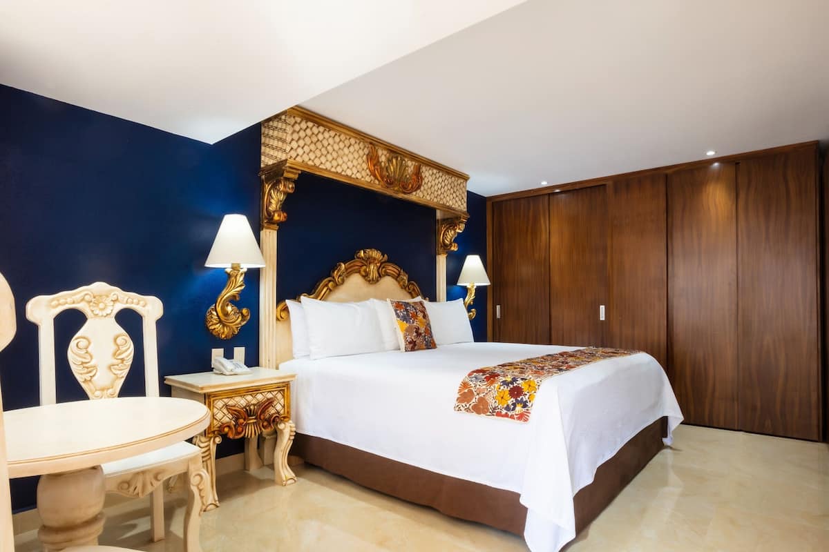 Une chambre d’hôtel avec un grand lit, une armoire en bois, une table de chevet avec une lampe et une chaise.