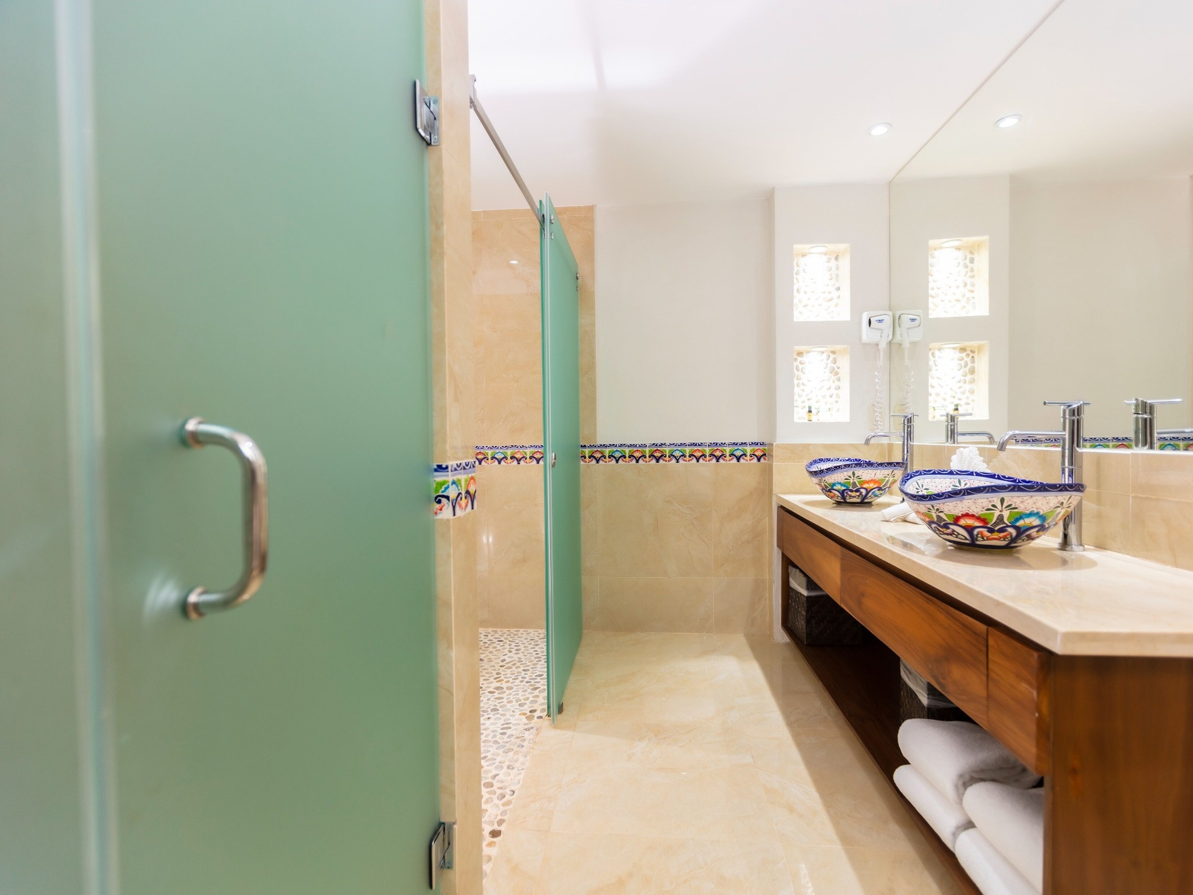 Um banheiro com chuveiro, pia com um recipiente decorativo, espelho e porta-toalhas.
