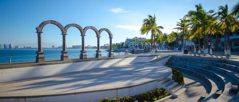 Un paseo marítimo con arcos de piedra, palmeras y vistas del horizonte de la ciudad.