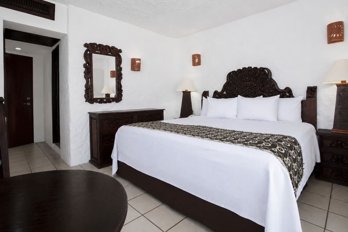Une chambre d’hôtel avec un lit, des tables de chevet, un miroir et une porte.