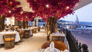 A restaurant with tables set for dining, a view of a bridge, and a beach in the background. - Playa Los Arcos Hotel Beach Resort & Spa (Puerto Vallarta)