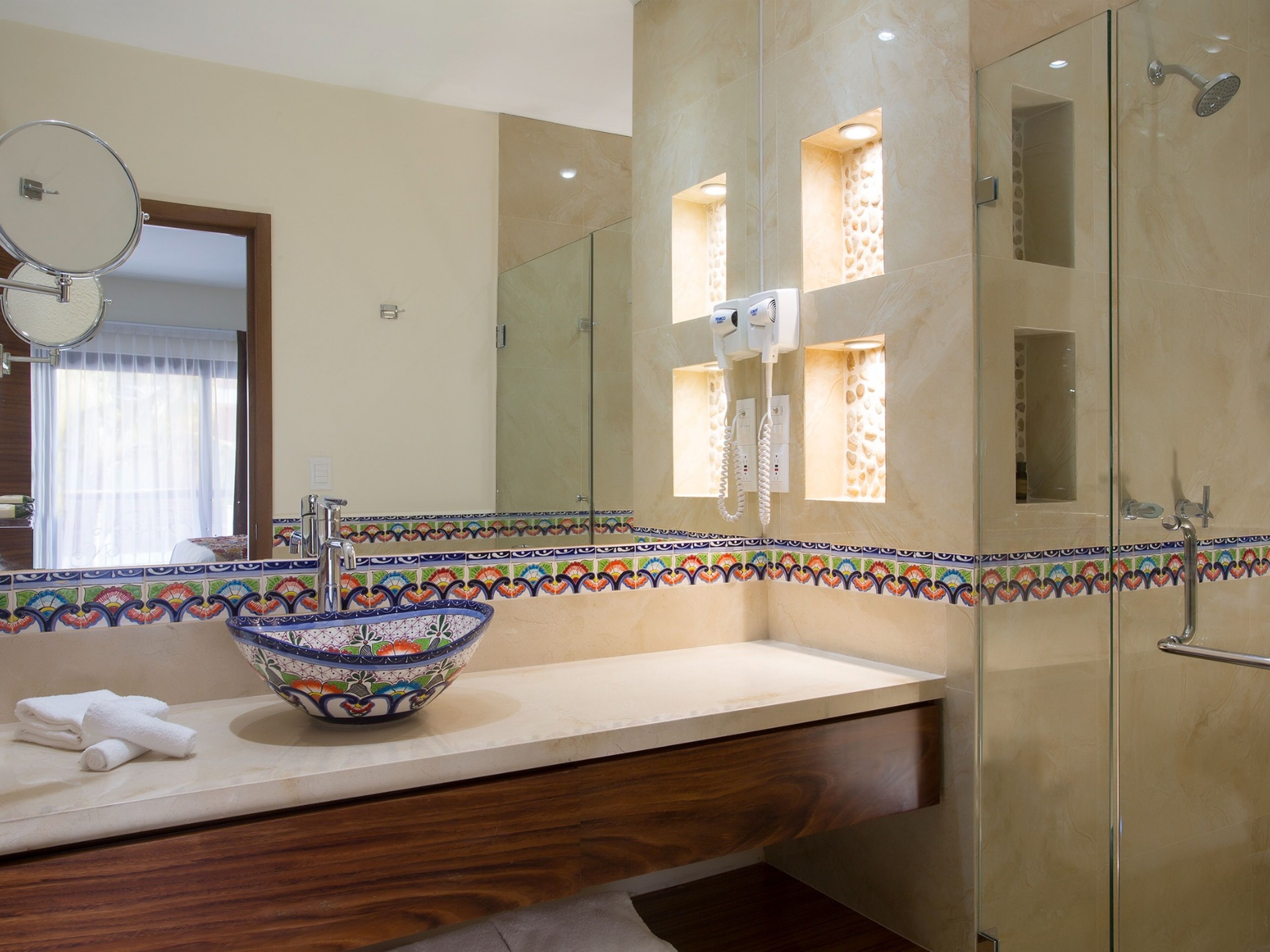 Um banheiro com um espelho grande, pia, chuveiro e uma borda de azulejos decorativa.