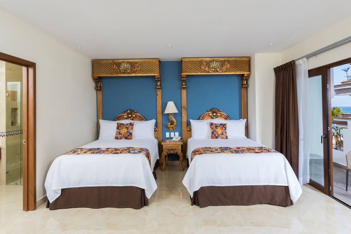 Une chambre d’hôtel avec deux lits, une table de chevet, une lampe et une vue sur la mer.