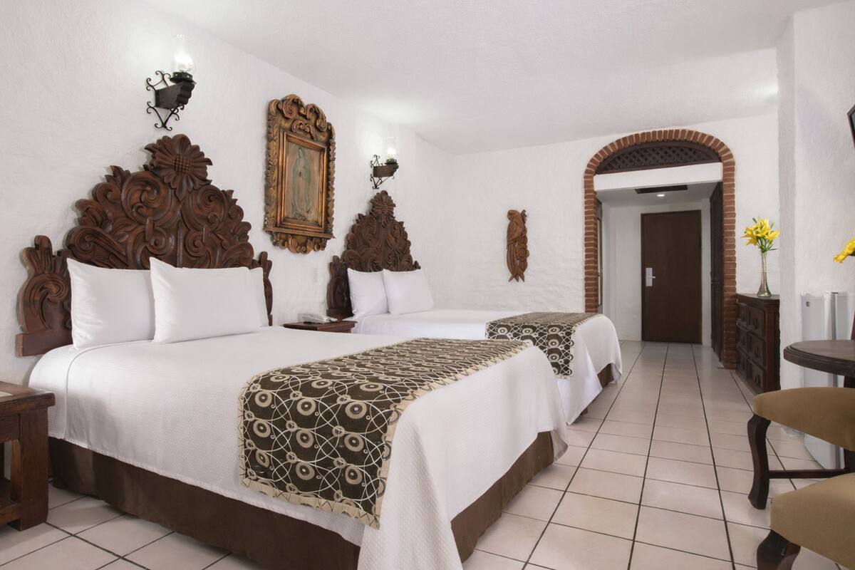 Une chambre d’hôtel avec deux lits, une tête de lit en bois, un tableau et une arche en briques.