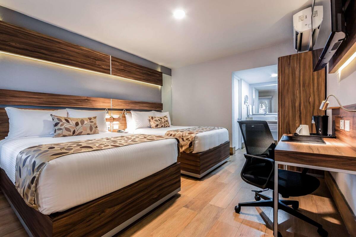 A modern hotel room with two beds, a wooden headboard, a desk, and a chair.