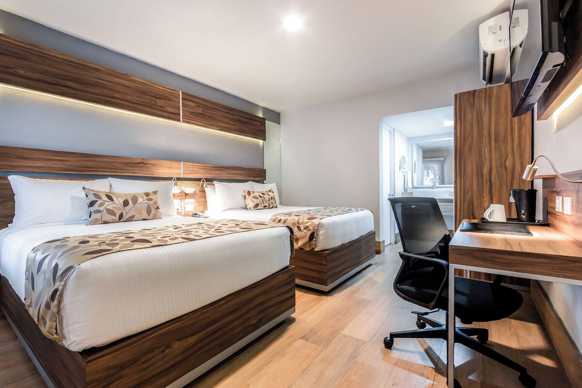 A modern hotel room with two beds, a desk, and a chair.