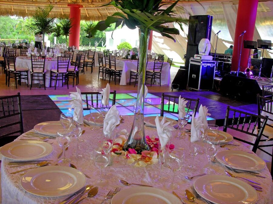 Un salón de banquetes con mesas redondas dispuestas para un evento formal, con manteles blancos, cubiertos dorados y centros de mesa florales.