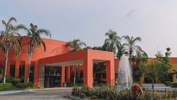 Um edifício moderno com fachada vermelha, palmeiras e uma fonte central.