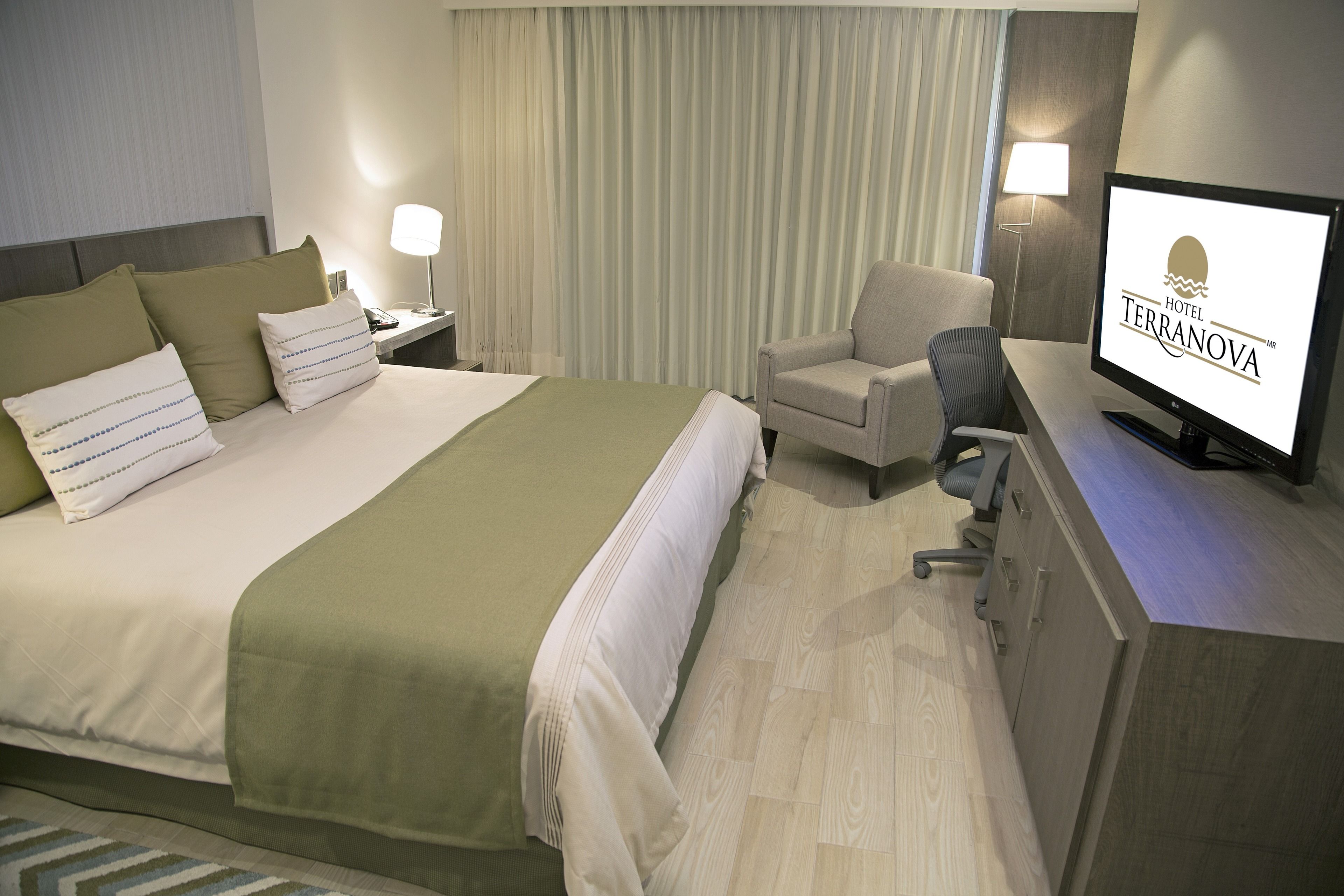 Habitación de hotel con cama, escritorio, silla, televisor y lámpara.