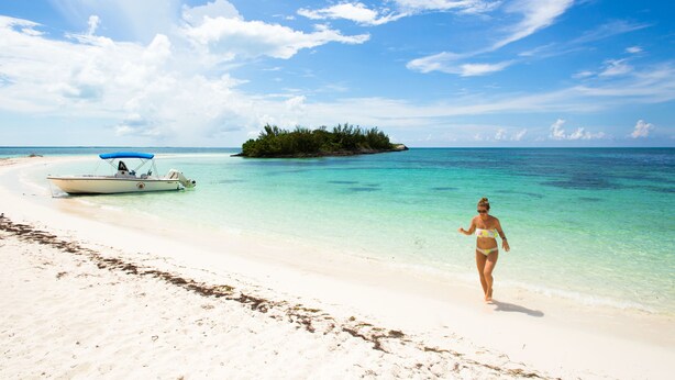 A beach with clear turquoise water, a boat, and a small island in the distance. - Green Turtle Club Resort & Marina (Green Turtle Cay)