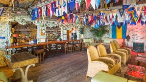 A bar area with wooden floors, wicker furniture, and a bar counter. Flags are hanging from the ceiling. - Green Turtle Club Resort & Marina (Green Turtle Cay)