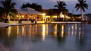 A waterfront restaurant with outdoor seating, palm trees, and a pool reflecting lights. - Green Turtle Club Resort & Marina (Green Turtle Cay)