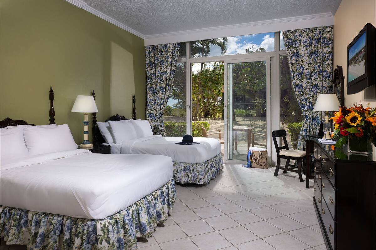 A hotel room with two beds, a desk, a chair, and a view of the outdoors.
