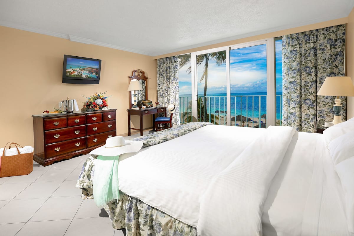 A hotel room with a bed, dresser, desk, and a view of the ocean.