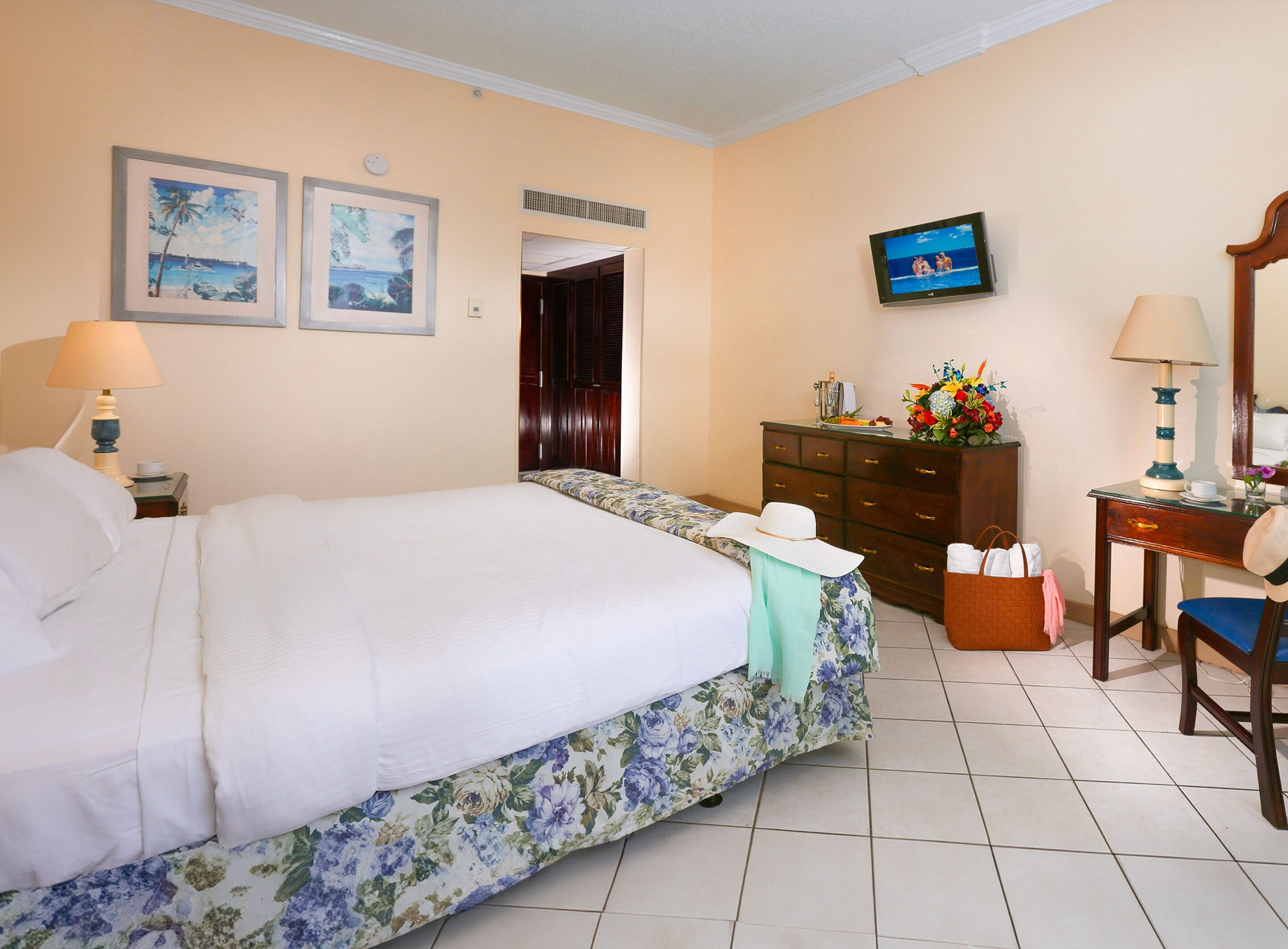Habitación de hotel con una cama grande, un aparador, un escritorio con silla, un televisor y dos cuadros en la pared.