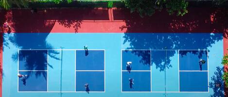 Vista aérea de una cancha de tenis con cuatro secciones, rodeada de árboles.