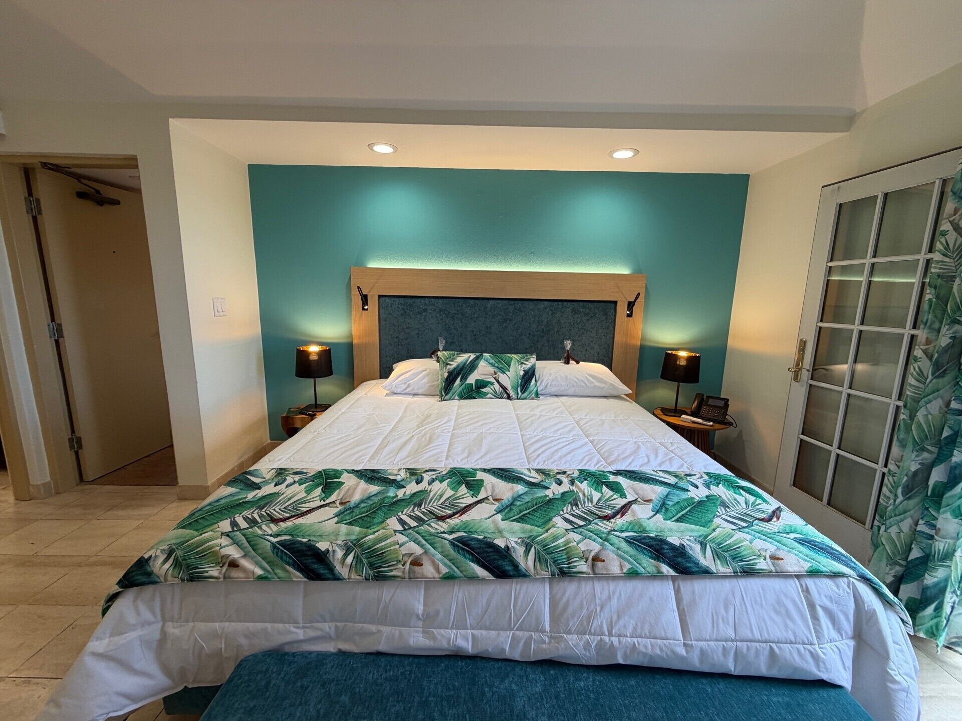 A hotel room with a large bed, two bedside tables, a wardrobe, and a door leading to another room.