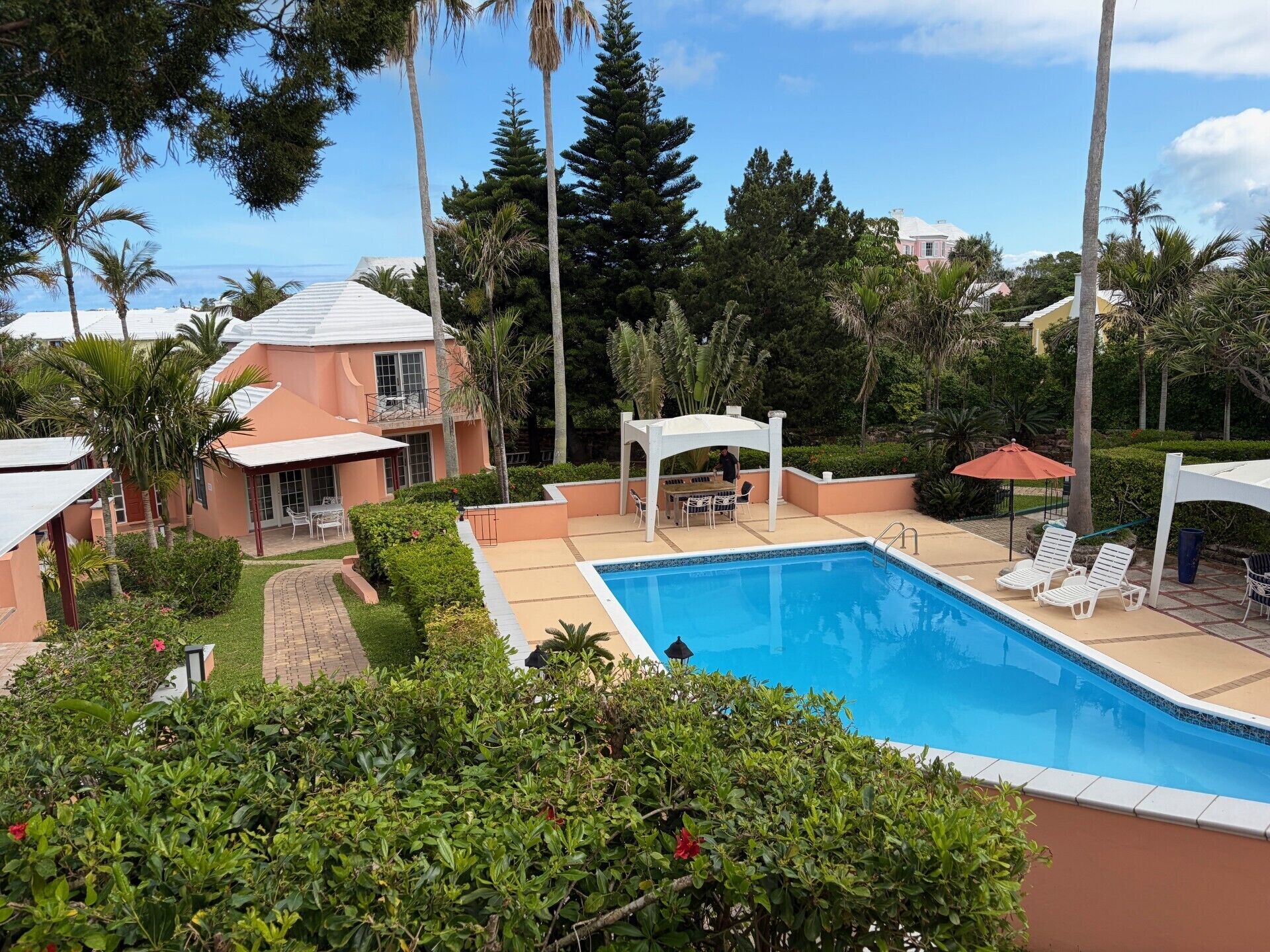 A swimming pool with lounge chairs, a covered patio, and a building with a sloped roof.