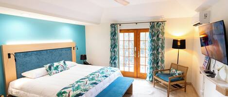 A bedroom with a bed, a bench, a chair, a ceiling fan, a TV, and a window with curtains.