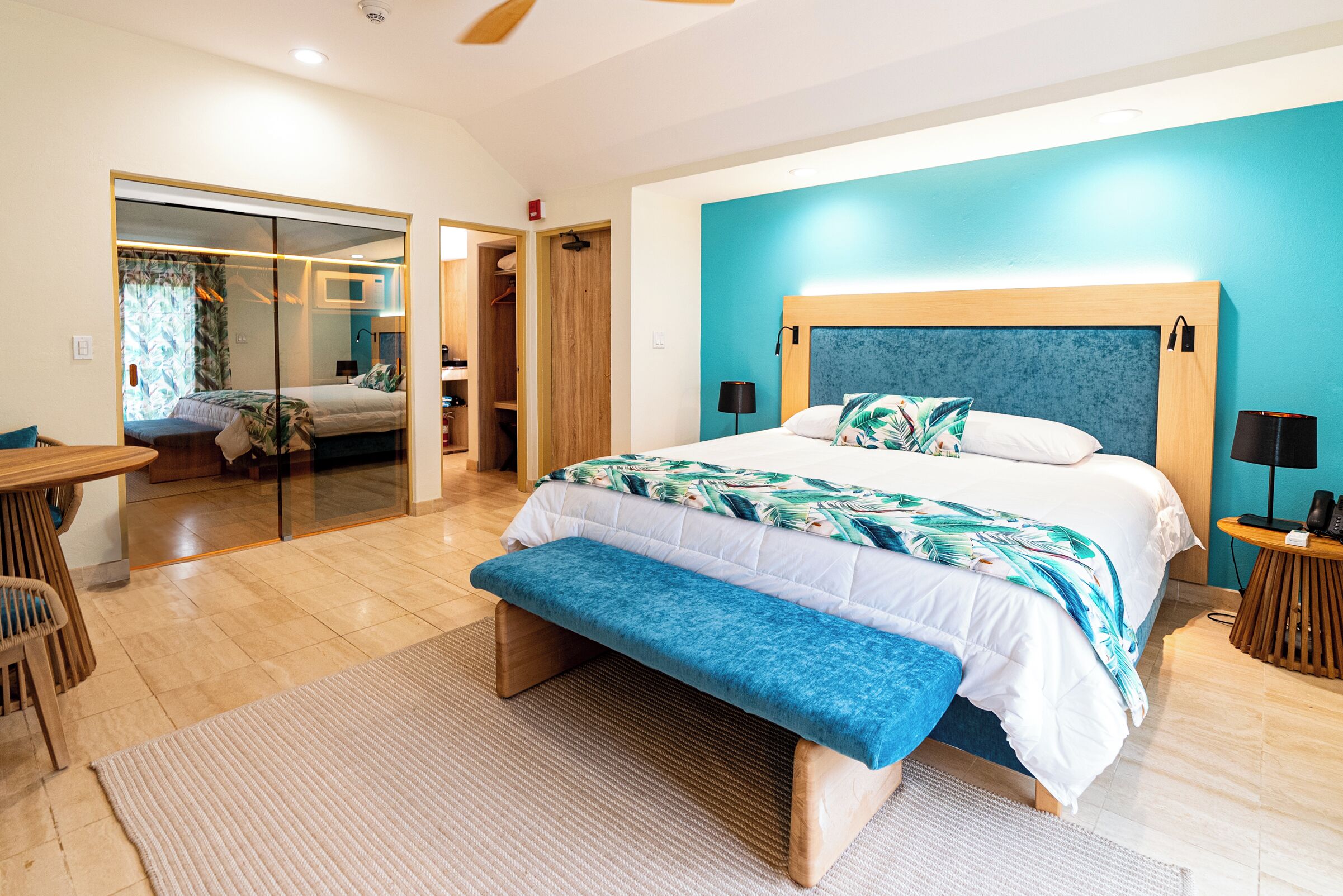 Quarto de hotel moderno com uma cama grande, um banco, uma escrivaninha e um closet espaçoso.