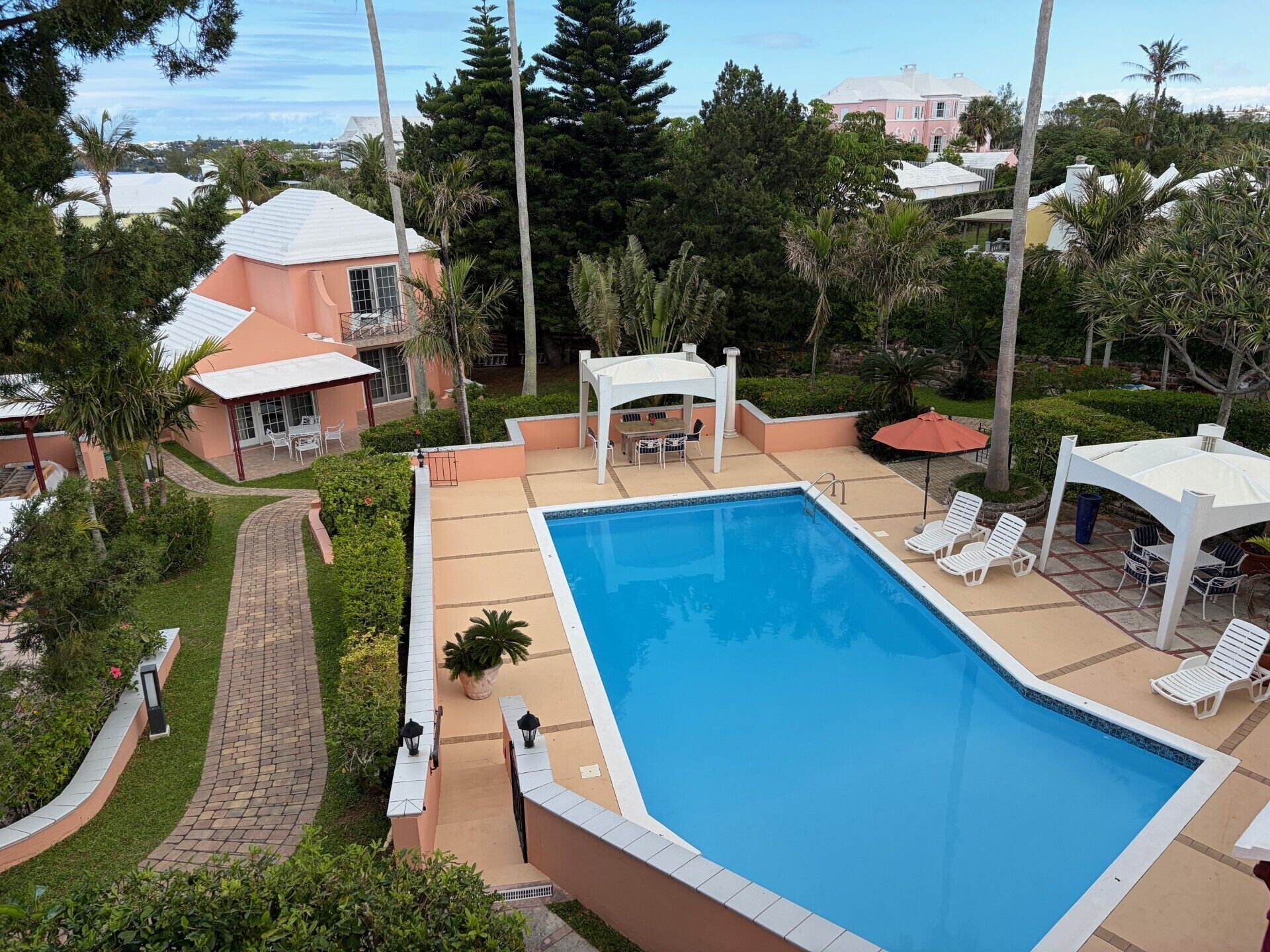A swimming pool with lounge chairs, a covered seating area, and a pathway leading to a building.