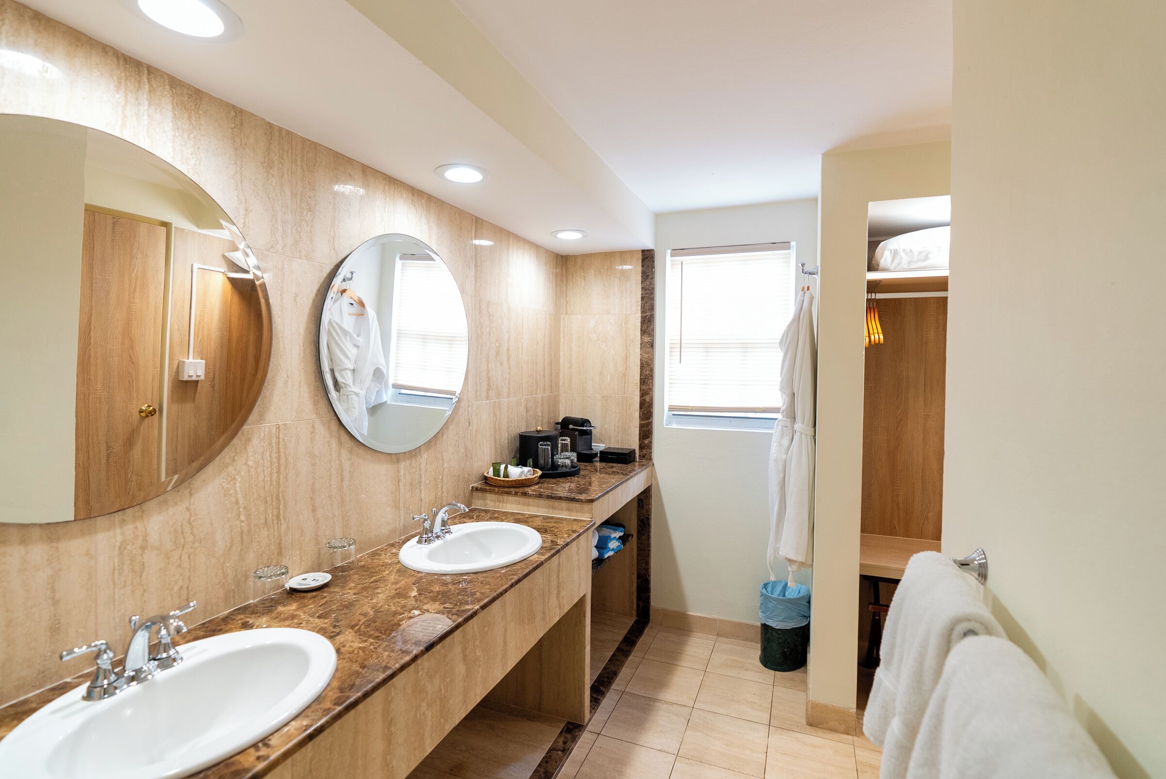 Une salle de bain avec deux lavabos, un grand miroir, un porte-serviettes et une fenêtre.