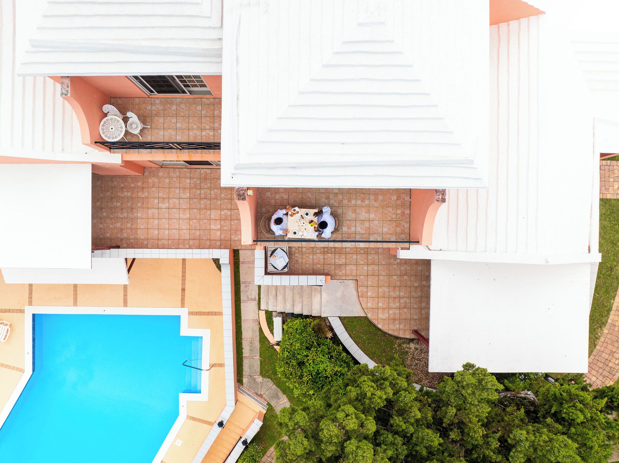 An aerial view of a residential property with a swimming pool, a patio with outdoor furniture, and a covered outdoor area.