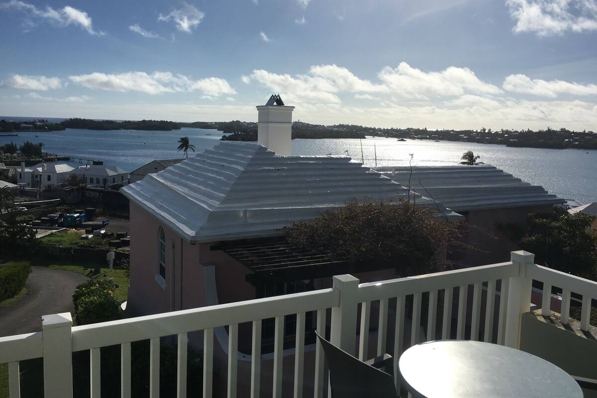 A residential building with a metal roof, a white fence, and a view of a body of water with boats.