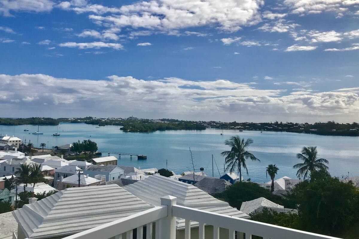 A coastal town with white buildings, a clear blue sky, and a calm sea with boats.