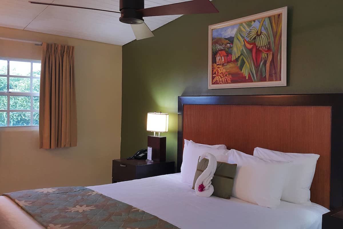 Habitación de hotel con una cama, una mesita de noche con lámpara, un cuadro en la pared y una ventana con cortinas.