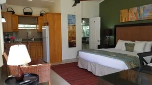 A compact hotel room with a bed, a small table with a lamp, a chair, a kitchenette, and a ceiling fan. - Blue Horizons Garden Resort (St. George's)