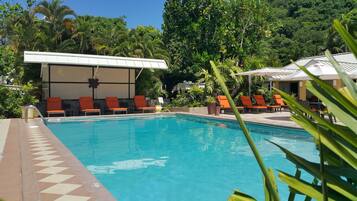 Una piscina con sillas de descanso naranjas y una zona de estar cubierta.