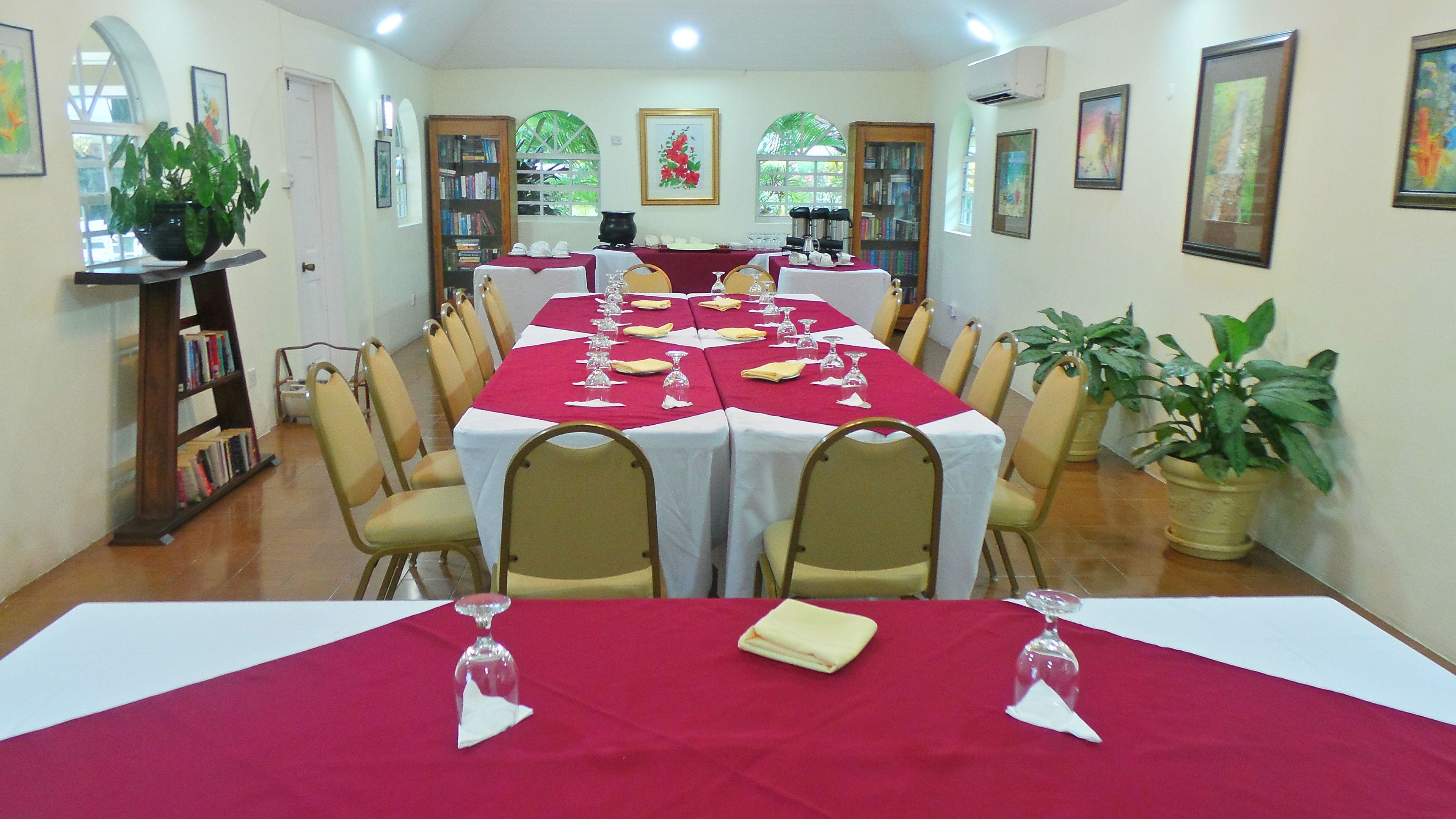 A dining area with tables set for a meal, chairs, a bookshelf, and a potted plant.